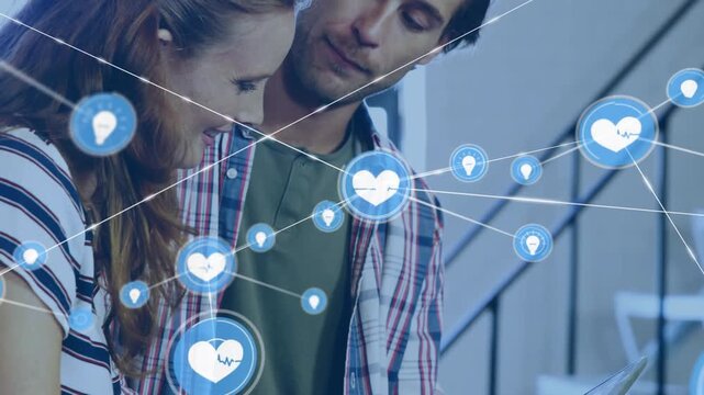 Pair standing by stairs, woman pointing tablet, blue icons forming network overlaying for marketing