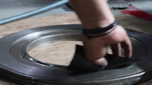 Close-up photo showing a mechanic's hand carefully sanding and smoothing the inner surface of an automatic transmission piston with sandpaper in a workshop environment.