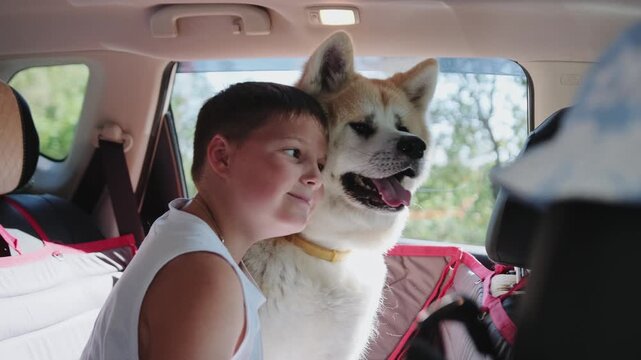 Smiling little boy hugging Akita Inu, sitting in the car on the back seat