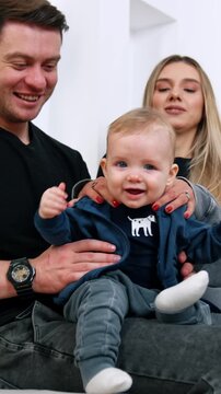 Happy blond baby boy in the parents' hands. Lovely family portrait of three at home.