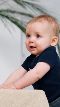 Lovely infant boy with red hair stands holding by the sofa. Cute little baby portrait.