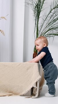 Cute smiling infant baby stands in the room. Adorable child trying to stand and walk alone.