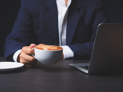 Business person holding coffee cup while working on laptop