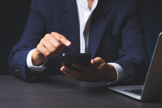 Business person using smartphone at desk with laptop
