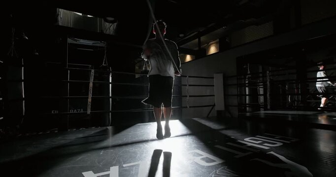 Man jumping rope during workout in the boxing ring. Athlete training with skipping rope, silhouette view. Fitness and cardio exercise. Dynamic shot