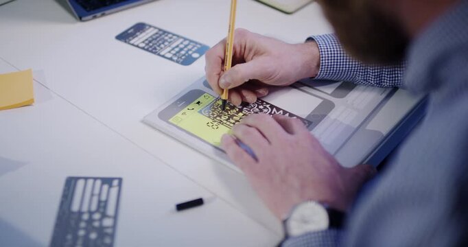 Close up of designer hands using pen and stencil to draw mobile app wireframes on paper in office