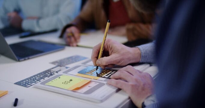 Close up of designer using pen and metal stencil to draw mobile app wireframes on paper during meeting