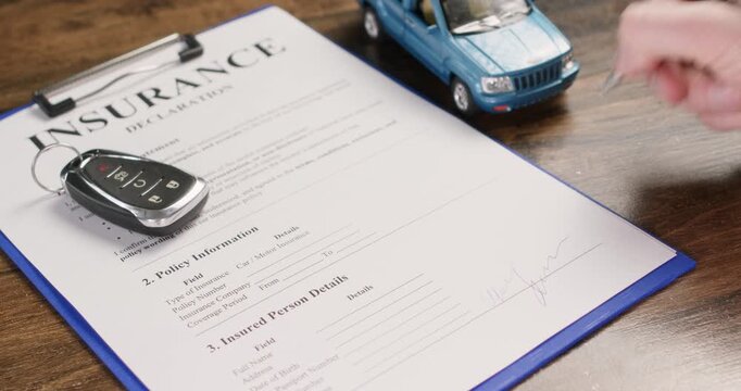 Car keys rest on insurance declaration as man signs policy form with hand. Driver puts signature completing coverage details during vehicle insurance process slow motion