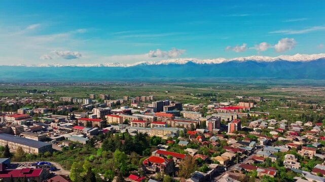 Drone aerial of Telavi, Georgia, revealing the city&rsquo;s rooftops, streets, and natural setting beneath the towering Caucasus mountains.