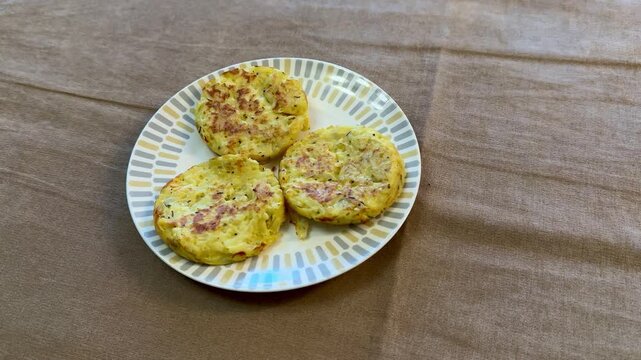Three potato pancakes on plate, crispy golden draniki seasoned with pepper and herb flakes, served on patterned ceramic plate.