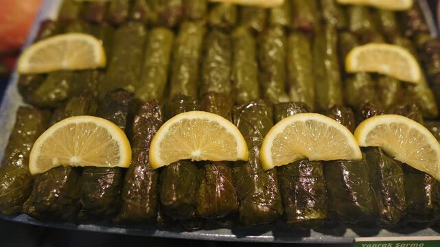 Closeup Tray Stuffed Grape Leaves Lemon Slices Arranged On Platter, Glossy Olive Oil Sheen Reveals Rice And Herb Filling, Bright Citrus Garnish Adds Zesty Contrast, Ideal For Mediterranean