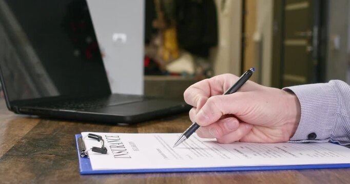 Manager hand fills out insurance policy near laptop at desk closeup. Professional agent checks financial document before client signature in company office