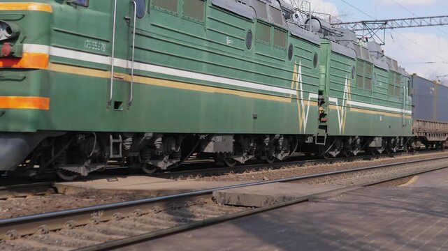 Freight Train Passing. Intermodal Freight Train Advancing Beside Station Platform Scene. Efficient Logistics Scene Capturing Cargo Train Passing Station With Detailed Chassis And Wheels