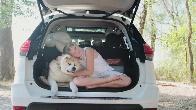 Happy kid hugging his Akita Inu dog while sitting in the open car trunk