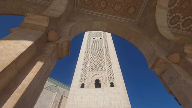 pan view of Hassan II Mosque against sky , Hassan II Mosque minaret looking up through arches - Hassan II Mosque minaret upward view through ornate arches Casablanca, Morocco