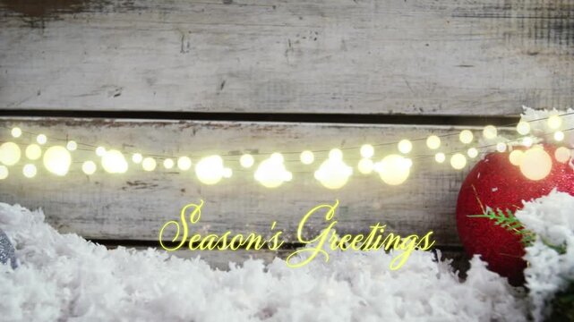 Animation of text, season's greetings, in yellow, over string lights, snow and christmas bauble