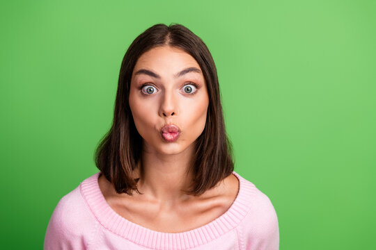 Young chic woman with pink sweater making a kissy face against a bright green background for fashion lifestyle stock photo