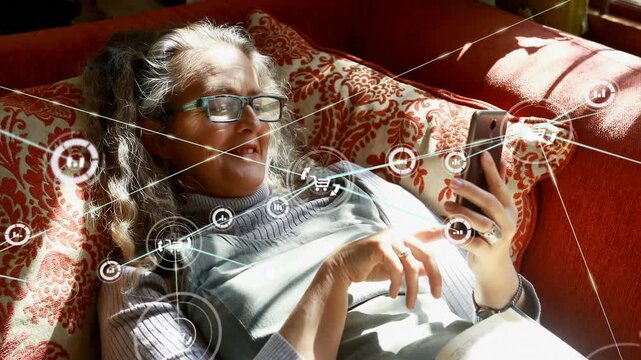 Application icons connecting with lines over caucasian senior woman using cellphone on sofa