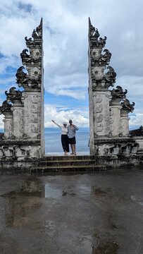 Happy Couple Posing at Balinese Candi Bentar Split Gate, Romantic Travel Moments at Ancient Hindu Temple with Water Reflection and Cloudy Sky