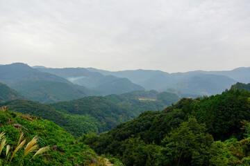 Obraz premium Expansive mountain valley with layered forested hills and mist along Shikoku Henro pilgrimage route in Japan
