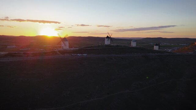 Consuegra windmills on a hill silhouetted against a golden sunset, with the Castle of La Muela in the background, a historic spanish landmark of Castilla La Mancha