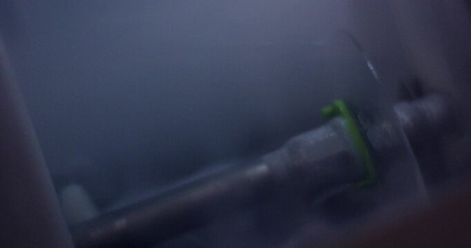 Close up of optical lens edger machine rotating an eyeglass lens behind a protective screen