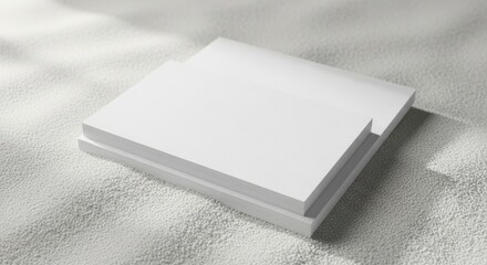 Fototapeta premium Two stacks of blank white business cards resting on a soft white grainy textured surface with natural sunlight and subtle shadows for branding product mockup design