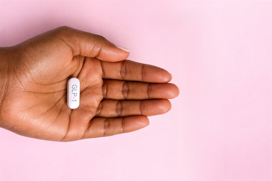 african american woman holding white glp-1 pill in hand. Weight loss medication and diabetes treatment concept. Pharmaceutical drug for metabolic health management and obesity control