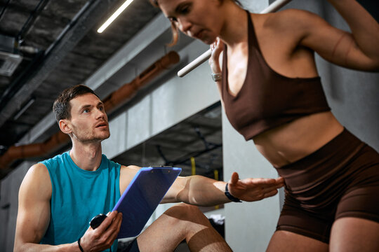 Man with clipboard analyzing woman movement during workout session. Concept of fitness analytics promotion, training app advertising, performance tracking branding and coaching business marketing
