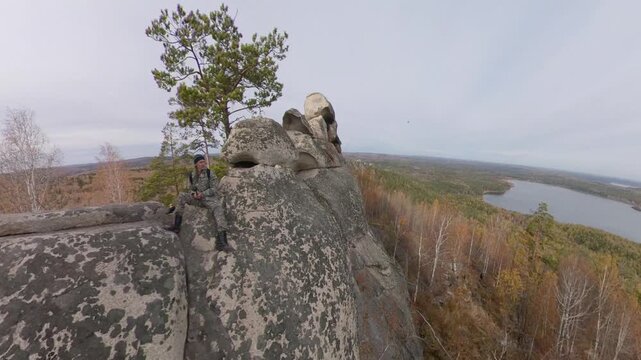 A man on a cliff. A hiker admires the picturesque autumn view of the forest and lake from a mountaintop, sitting on granite rocks.