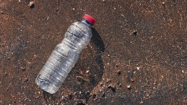 Plastic bottle on a sandy beach washed by ocean waves in slow motion. Environmental pollution concept, marine debris, plastic waste, ocean conservation, coastal cleanup, ecological problem, nature 