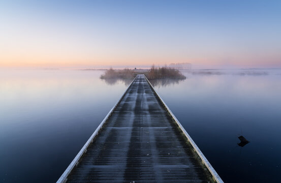 Wooden footbridge over a lake during a foggy and cold, spring morning in the Netherlands.