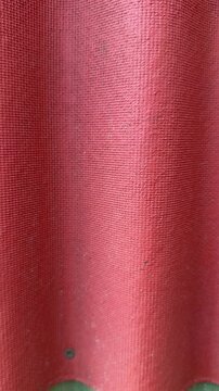 Red ondulin roofing close up corrugated. Fine grain bitumen surface with repeating waves, sunlight highlights, weatherproof.