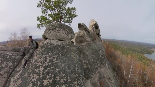A man on a cliff. A hiker admires the picturesque autumn view of the forest and lake from a mountaintop, sitting on granite rocks.