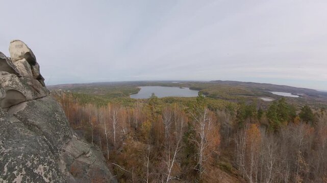A man on a cliff. A hiker admires the picturesque autumn view of the forest and lake from a mountaintop, sitting on granite rocks.