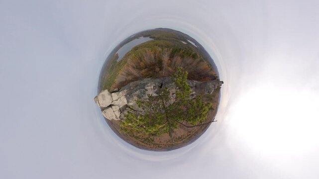 Rocks, forest, and lakes in autumn. View of a small planet. A granite cliff with a pine tree growing on its summit and a panoramic view of a mixed forest and lakes in the distance. 360 degree camera.