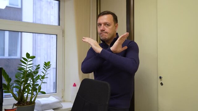 Determined male professional in contemporary office setting performs clear stop gesture, conveying refusal or prohibition with serious demeanor.