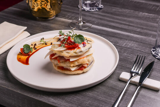 Millefoglie di pesce fritto, sugo di pomodoro, scaglie di formaggio e pomodori confit accompagnata da un calice di vino bianco e servita in un ristorante elegante
