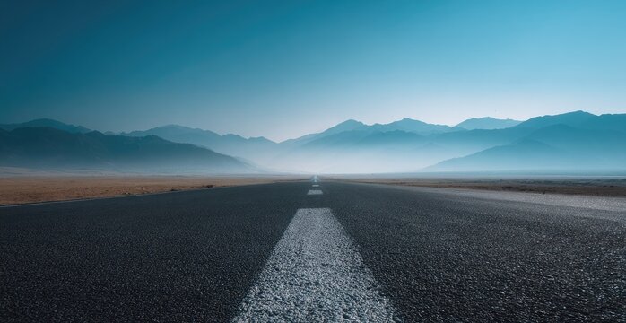 Endless asphalt road stretching towards hazy mountains under a vast blue sky
