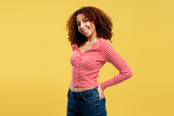 Young woman with curly hair smiling and posing on yellow background