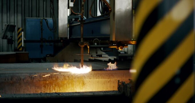 Automatic CNC laser machine cutting a thick metal plate with bright sparks and fire in a factory