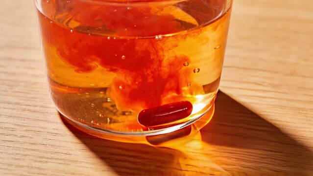 Close-up of orange tonic glass with astaxanthin supplement diffusing glowing skin elixir