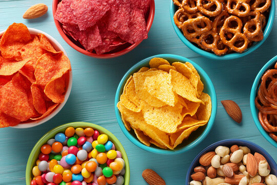 Colorful snack assortment with chips pretzels nuts and dip on blue wooden background with copy space