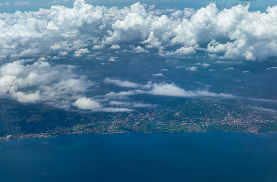 Aerial view of Bali coastline with villages, farmland and shoreline under scattered clouds.