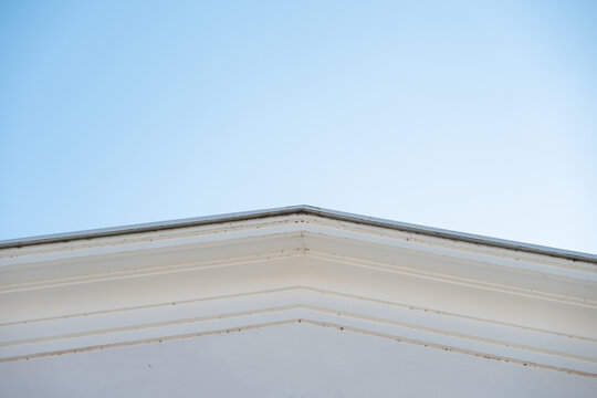  Classic white architectural cornice against a clear blue sky . Geometric lines of a white pediment. Concept of classic architecture and minimalism.
