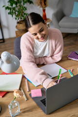 Teen girl happily using her laptop in a cozy apartment, embracing creativity © LIGHTFIELD STUDIOS