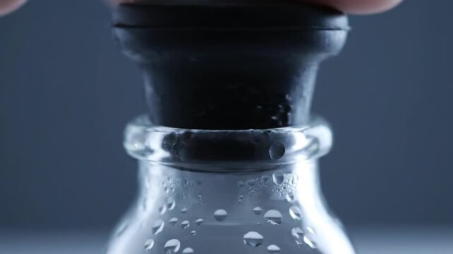 Close-up of a finger pressing down on a black rubber stopper on a wet glass bottle