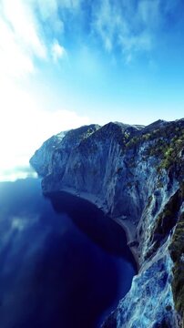 Spectacular landscape featuring stunning cliffs alongside calm waters under a clear blue sky. The sun reflects beautifully on the waters surface, creating a tranquil atmosphere.