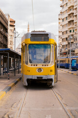 Fototapeta premium Vintage yellow tram moving through historic city street in Alexandria Egypt