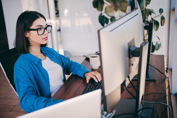 Businesswoman at a computer in a modern office focused on programming and work with a large monitor...